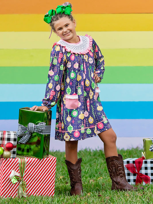 Navy smocked ornament-themed dress on a little girl standing next to a pile of Christmas presents.