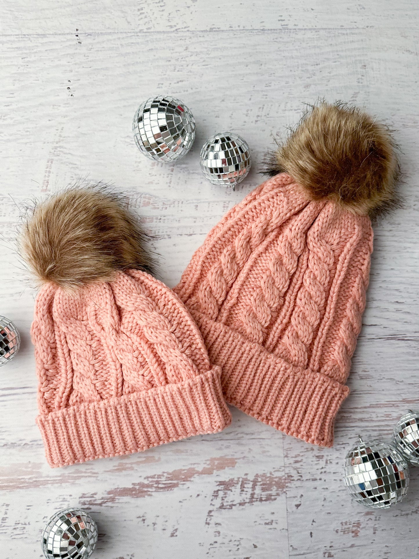 Matching mommy & me knit beanies in light pink with brown fur top knots.