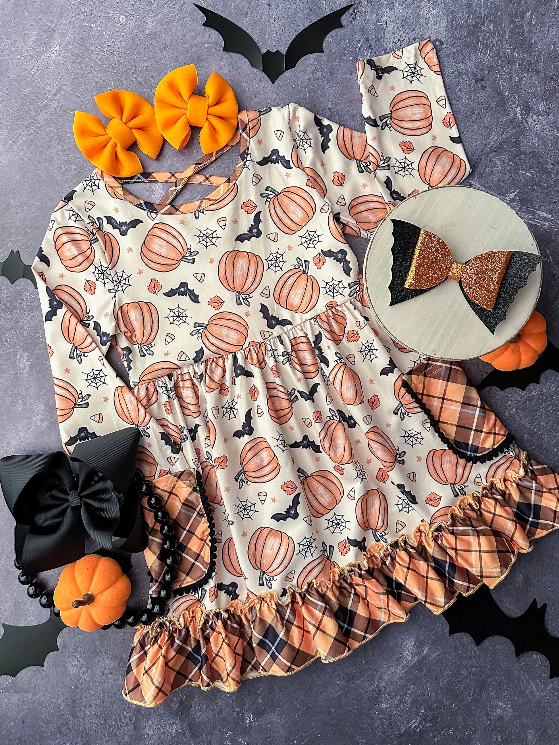 Long sleeve dress in a pumpkin & bat print with flannel print pockets and ruffle detailing.