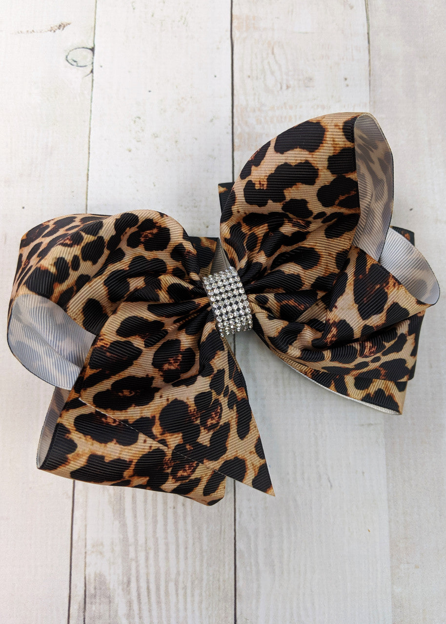 A large double looped grosgrain leopard print ribbon hair bows with an elegant 1/2" strip of six rows of tiny rhinestones around the center.  Attaches with a large 3" alligator clip with "teeth" for a secure hold.  The bow measures approximately 6.5" long and 5" wide.