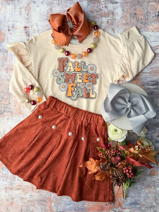 Long sleeve cream top with ruffled shoulders and a design that reads 'Fall sweet fall'; coordinating rust-colored skirt with pearl embellishments.