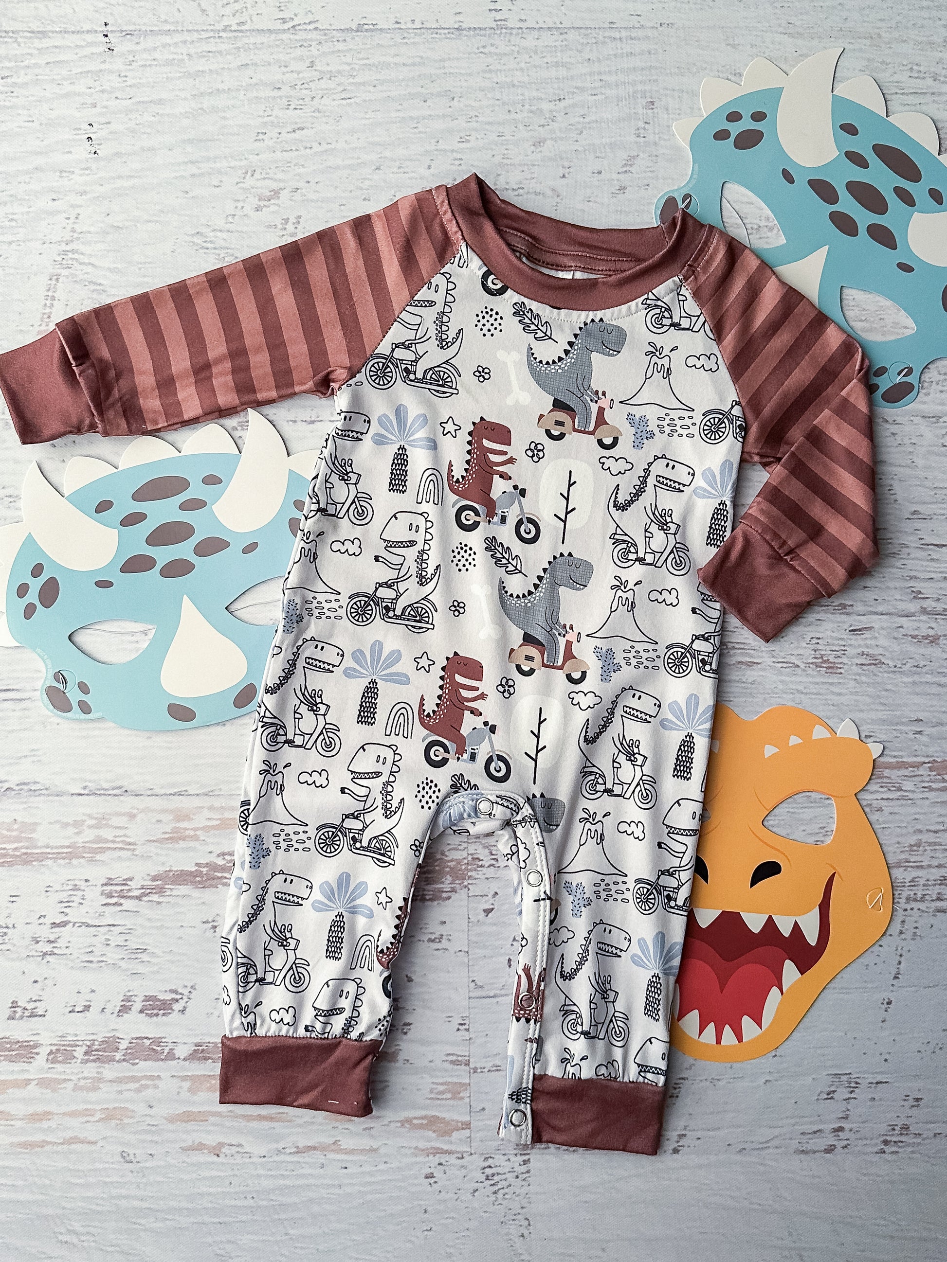 Long sleeve Dino print infant romper with a layered look, brown striped sleeves and snap closure.