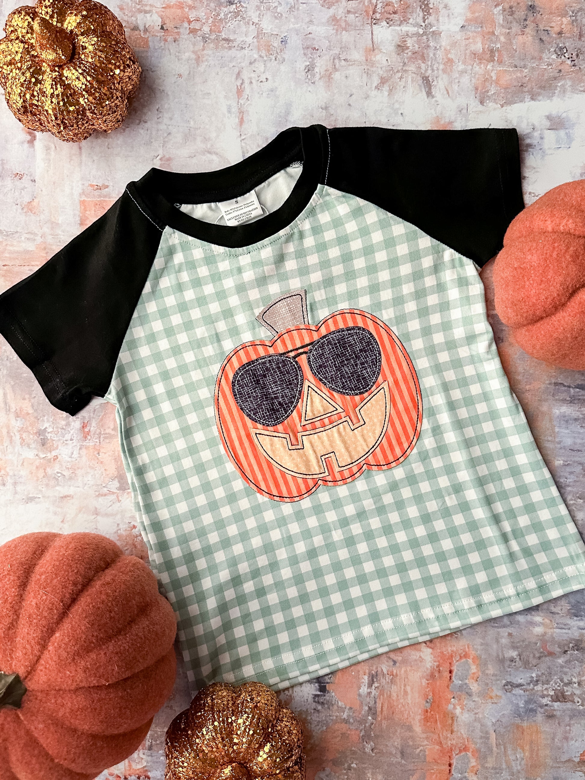 Green gingham shirt with black short sleeves and a pumpkin appliqué.