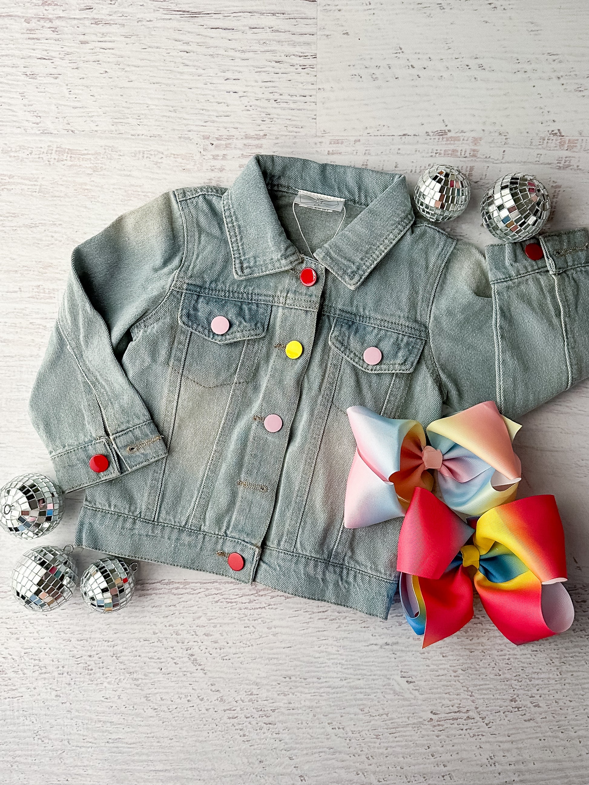 Jean jacket with colorful buttons; the back features a sequin rainbow with colorful fringe hanging from the clouds.