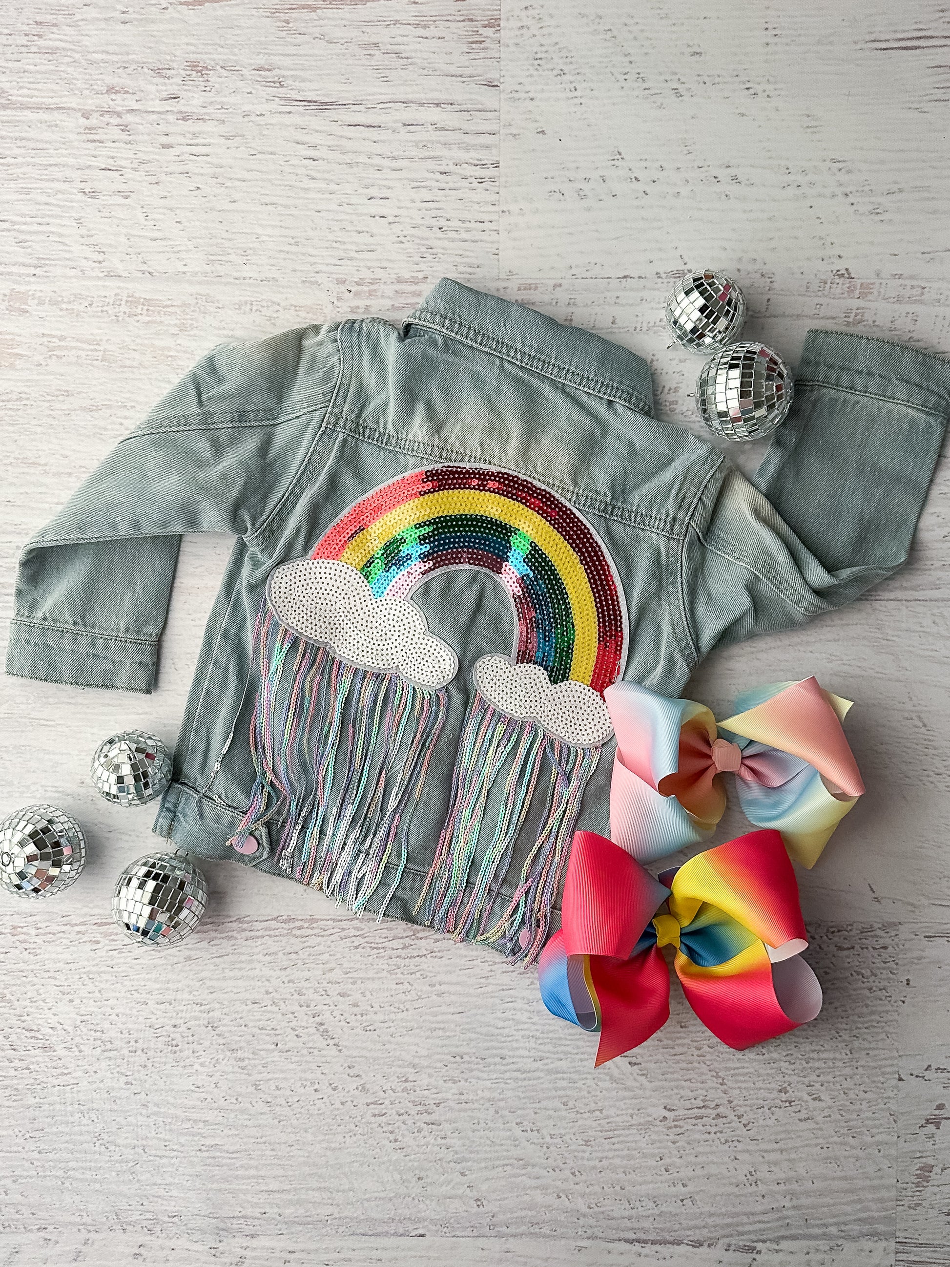 Back of jacket shown, featuring a sequin rainbow with colorful fringe hanging from the clouds.