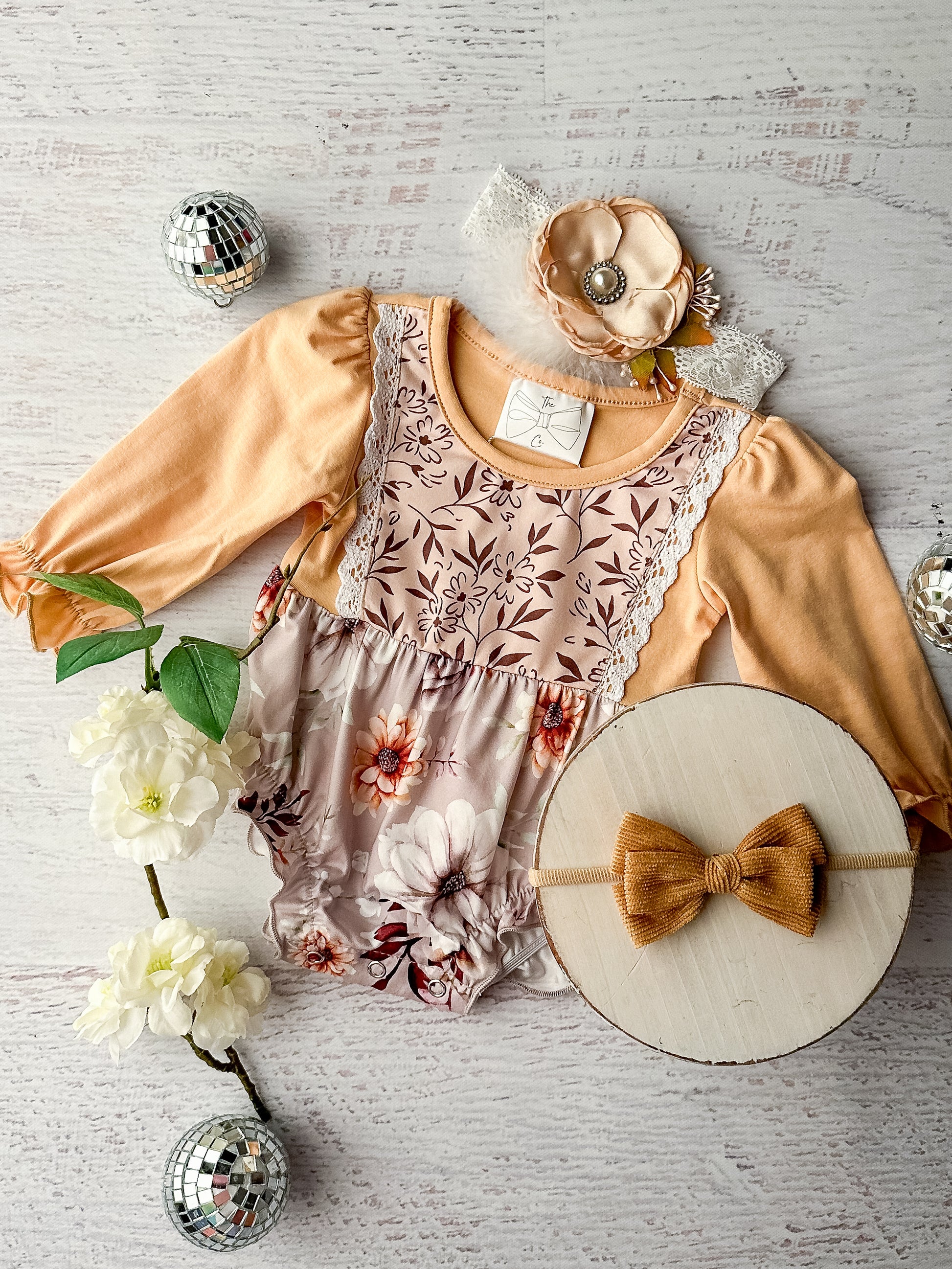 Golden yellow long sleeve infant romper with lace detailing and a brown and tan floral print fabric.