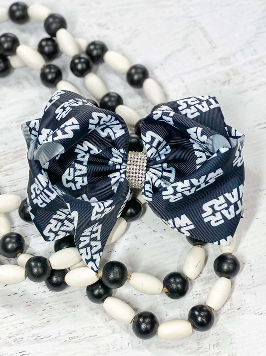 A large double looped black Star Wars print grosgrain ribbon hair bow with an elegant 1/2" strip of six rows of tiny rhinestones around the center.  Attaches with a large 3" alligator clip with "teeth" for a secure hold.