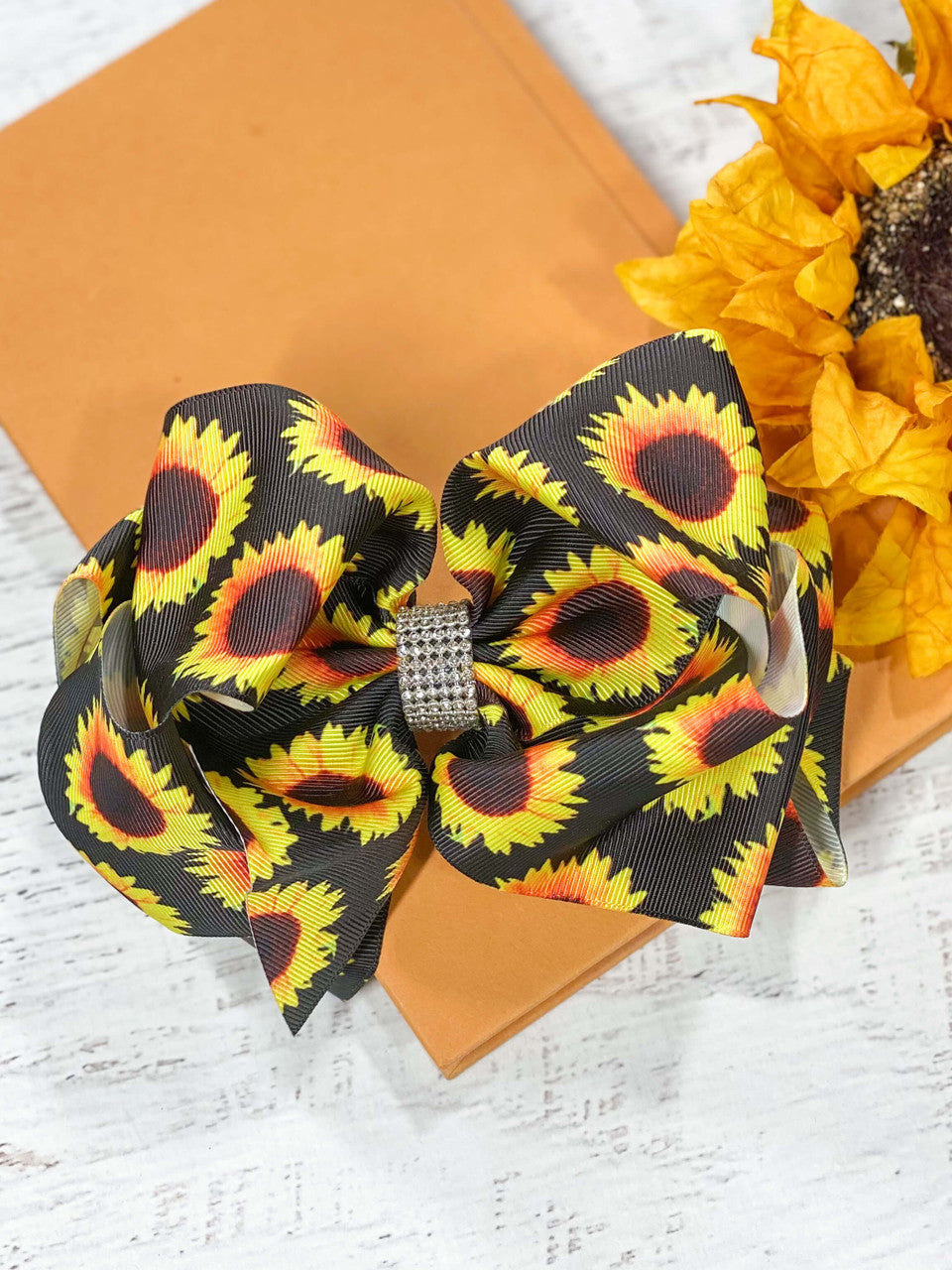 A large double looped sunflower print grosgrain ribbon hair bows with an elegant 1/2" strip of six rows of tiny rhinestones around the center.  Attaches with a large 3" alligator clip with "teeth" for a secure hold.  The bow measures approximately 6.5" long and 5" wide.