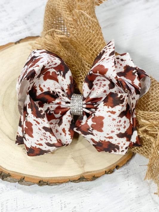 A large double looped brown, black, and white cowhide print grosgrain ribbon hair bow with an elegant 1/2" strip of six rows of tiny rhinestones around the center.