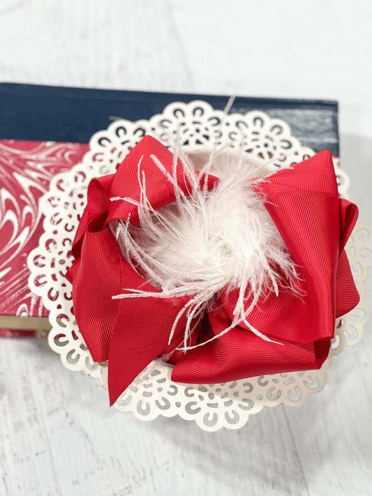 A large double looped red grosgrain ribbon hair bows with a white ostrich puff center.  Attaches with a large 3" alligator clip with "teeth" for a secure hold.  The bow measures approximately 6.5" long and 5" wide.