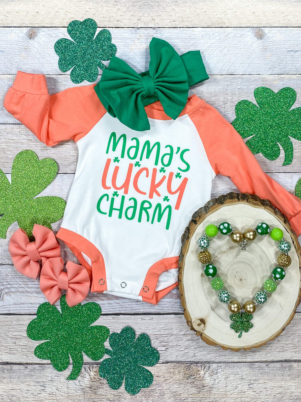 Coral long sleeves on a white bodice onesie that reads 'Mama's lucky charm'.