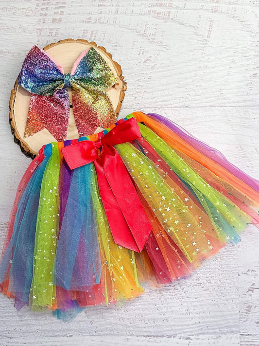 Rainbow sparkle tie tutu featuring assorted colors of glitter tulle looped over an elastic waistband with a hot pink bow accent.