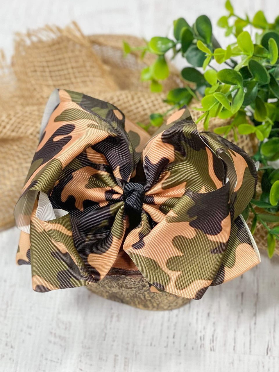 A large double looped grosgrain ribbon hair bow in a camouflage print with a black center knot.