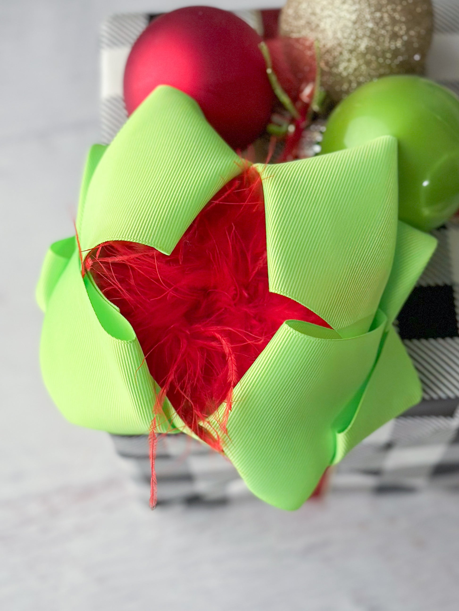 A lime green large double-looped grosgrain ribbon hair bow with a red ostrich feather puff in the center.