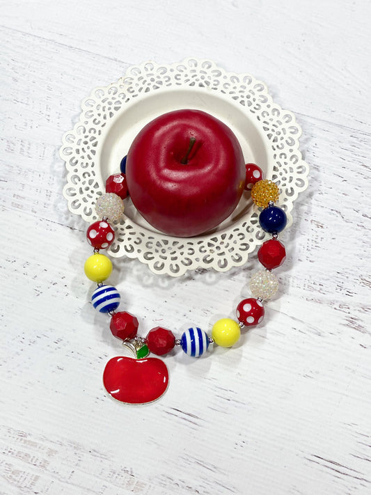 Red apple pendant chunky bead necklace with red polka dot, blue and white striped, white rhinestone, solid red, blue, and yellow beads, with a heart toggle closure.