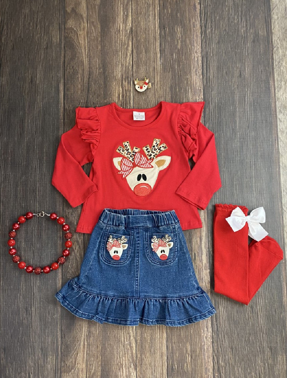 This red cotton top features an adorable red nosed reindeer with animal print antlers applique and ruffled shoulders. The denim skirt is ruffled with reindeer on the pockets. 